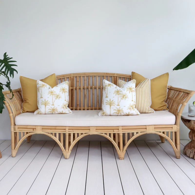 mustard-outdoor-sofa-cushions-set-5-covers-colo1171 A set of 5 mustard outdoor cushions sits on a rattan seat nestled against a white wall.