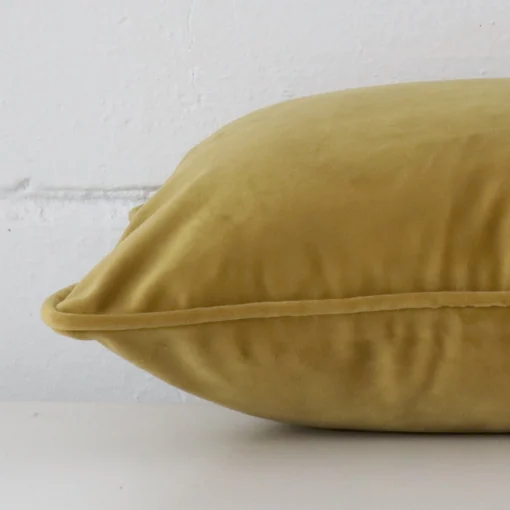 A rectangle mustard cushion cover laying flat. This viewpoint highlights the velvet fabric from a side position.