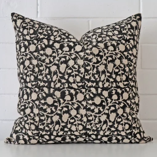 Floral cushion positioned in front of a brick wall. It has large dimensions and is made from a designer material.