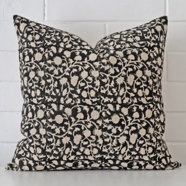 Floral cushion positioned in front of a brick wall. It has large dimensions and is made from a designer material.