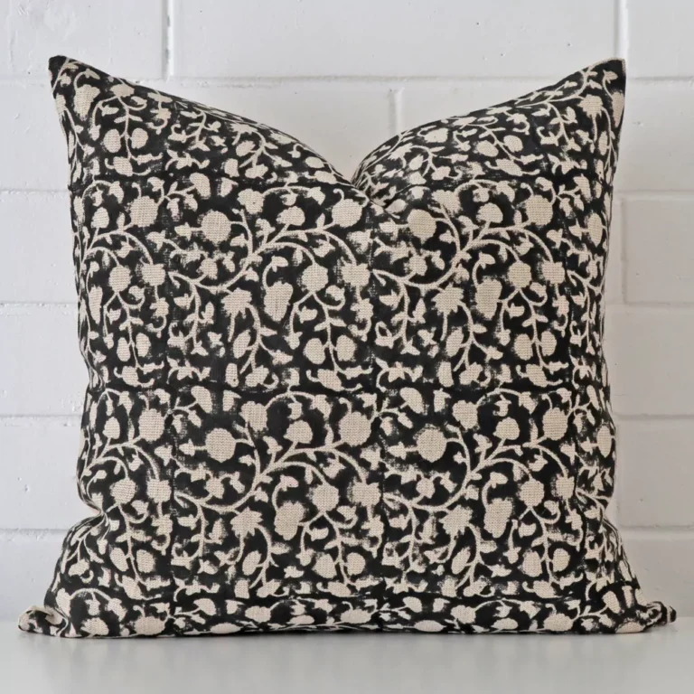 Floral cushion positioned in front of a brick wall. It has large dimensions and is made from a designer material.
