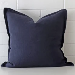 A lovely large navy cushion cover arranged in front of a white wall. It is made from a linen material.
