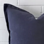 Enlarged shot of the corner of this large cushion cover in navy colour is shown against a brick wall. The image shows the quality and craftsmanship of the linen material.
