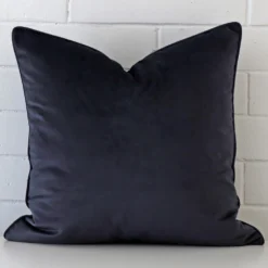 Navy cushion leans elegantly against a brick wall. It has been crafted from a high quality material and has a large shape.