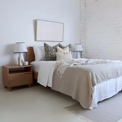 An airy white bedroom with 4 designer bed cushions sitting on a wooden bed.