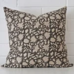 Floral cushion positioned in front of a brick wall. It has large dimensions and is made from a designer material.