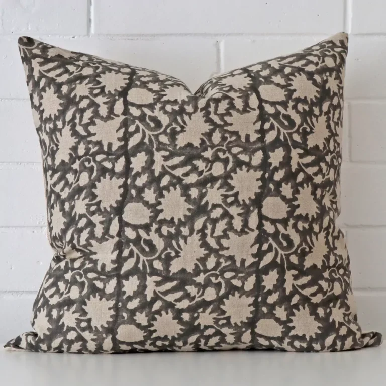 Floral cushion positioned in front of a brick wall. It has large dimensions and is made from a designer material.