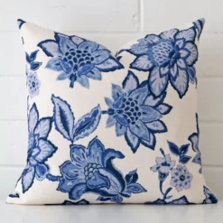 A lovely square cushion cover arranged in front of a white wall. The floral style complements the linen material.