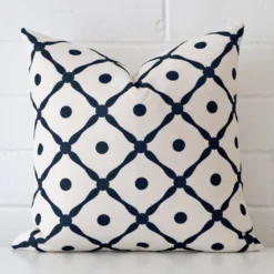 Cushion positioned in front of a brick wall. It has square dimensions and is made from a linen material.