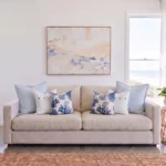 Six cushions in pairs of sky blue linen, button detail, and coral print, on a sofa.