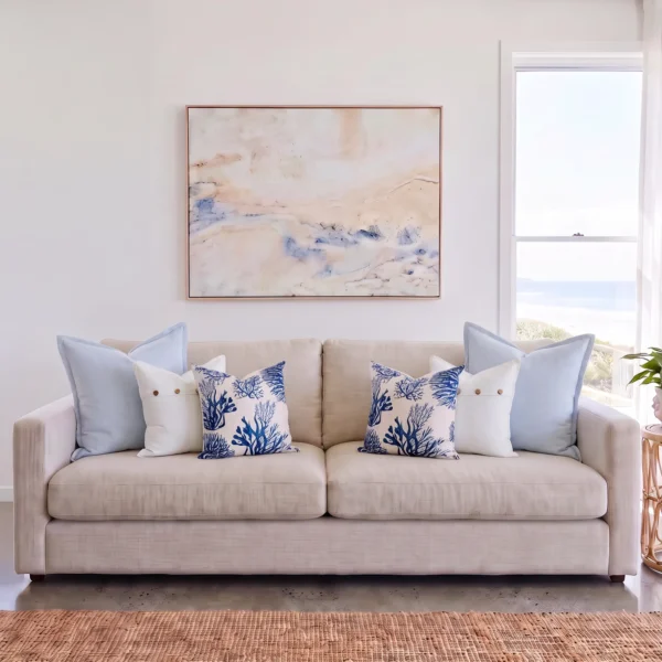 Six cushions in pairs of sky blue linen, button detail, and coral print, on a sofa.
