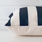 A striped cushion cover is laid flat. This angle shows the side of the linen fabric and its square shape.