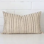 A designer rectangle cushion cover that has a unique striped design is shown vertically against a brick wall.