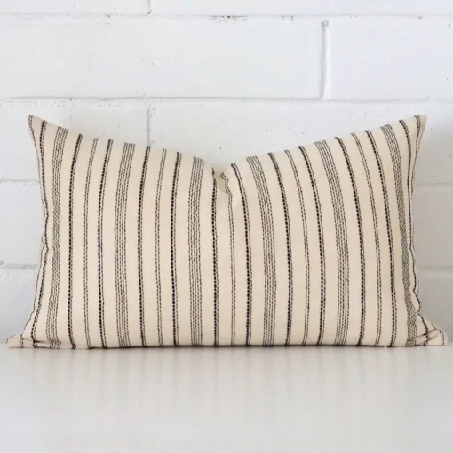 A designer rectangle cushion cover that has a unique striped design is shown vertically against a brick wall.