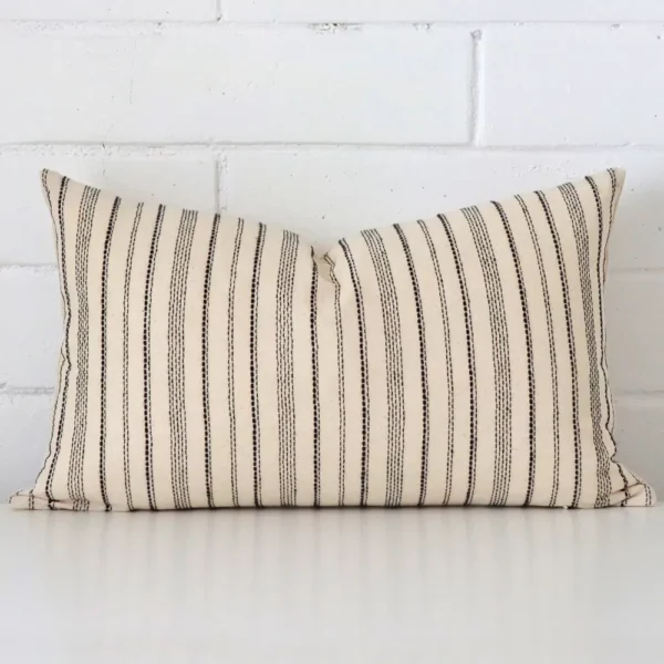 A designer rectangle cushion cover that has a unique striped design is shown vertically against a brick wall.