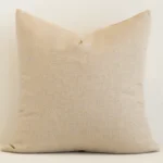 Square solid-coloured cushion cover in natural colour sitting upright in front of a wall. It has been made from a quality linen material.