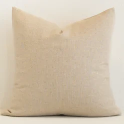 Square solid-coloured cushion cover in natural colour sitting upright in front of a wall. It has been made from a quality linen material.