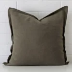 Olive cushion positioned in front of a brick wall. It has large dimensions and is made from a linen material.