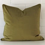 A pretty velvet cushion cover is shown against a brick wall. It features a large shape and an olive colour finish.