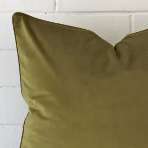 Enlarged shot of the corner of this large cushion cover in olive colour is shown against a brick wall. The image shows the quality and craftsmanship of the linen material.