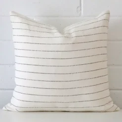A lovely square cushion cover arranged in front of a white wall. The striped style complements the linen material.