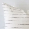 A zoomed in photo of the corner of a striped cushion that has linen fabric and a square size.