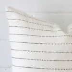 A zoomed in photo of the corner of a striped cushion that has linen fabric and a square size.