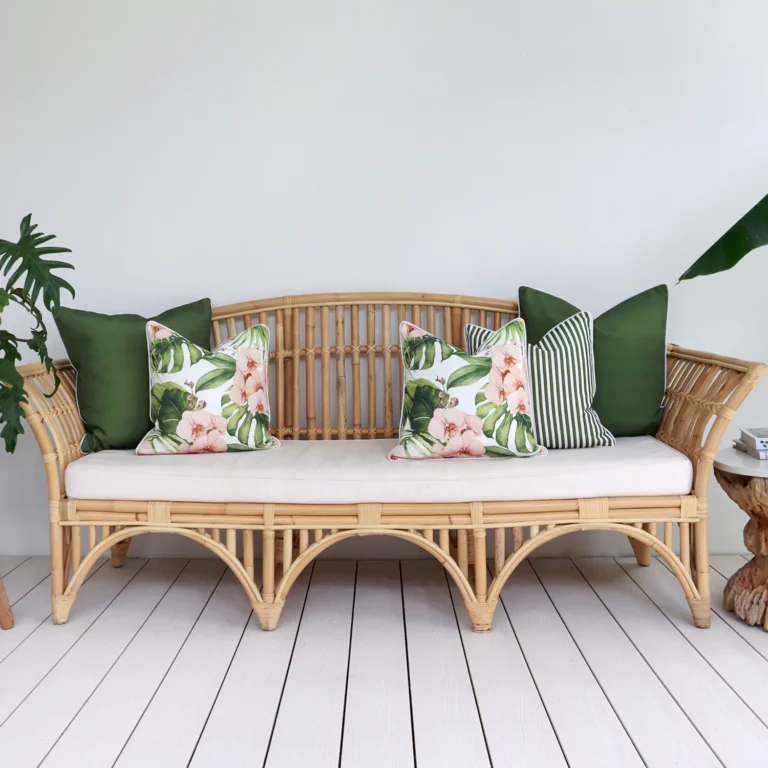 A set of 5 olive outdoor cushions sits on a rattan seat nestled against a white wall.