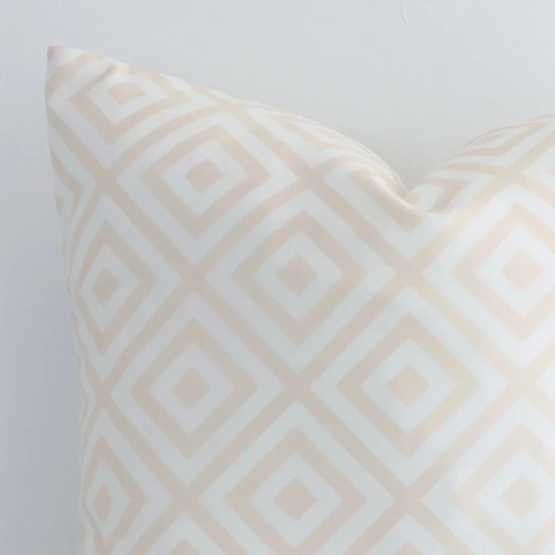 Close range image of white and beige geometric cushion. The square size and outdoor material can be seen in detail.