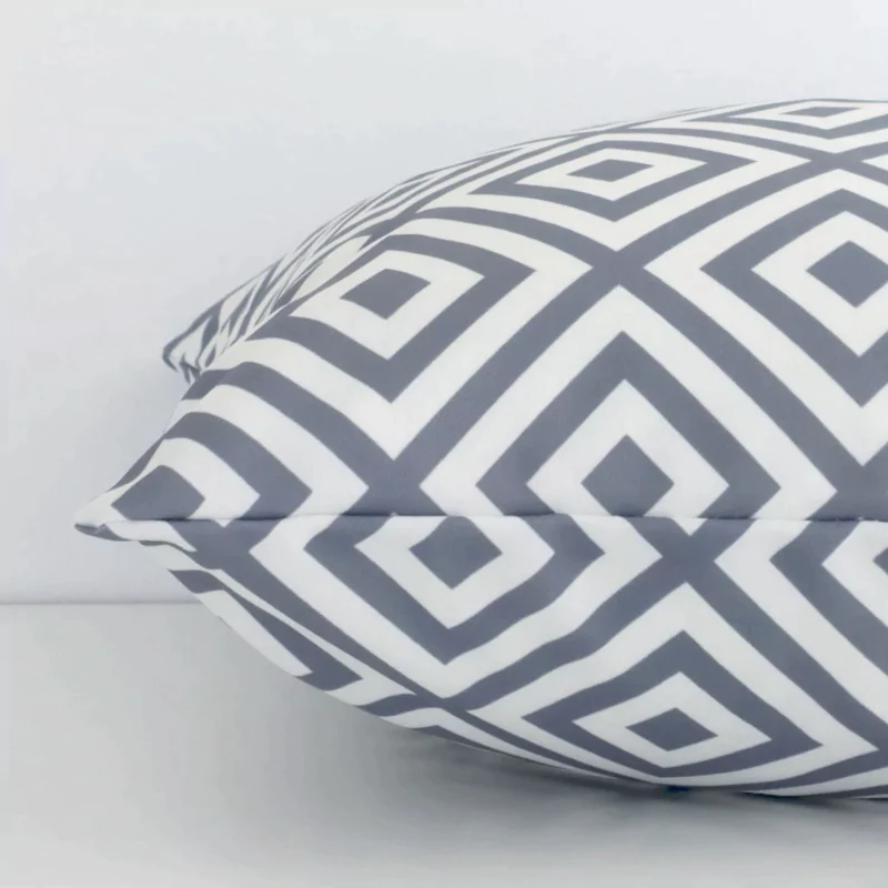 Side perspective showing seam of square white and grey cushion cover that has a geometric motif on its outdoor fabric.