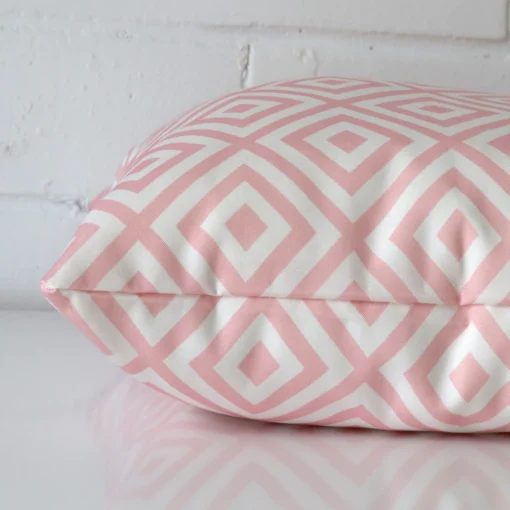 Side angle of pink geometric cushion cover that has outdoor fabric and a square size.