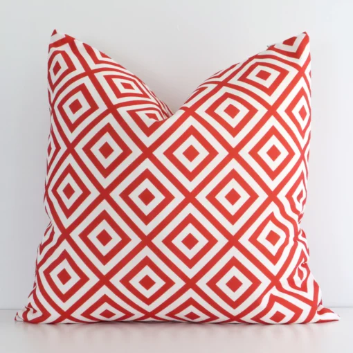 White wall with an orange geometric cushion laying against it. It has a distinctive outdoor fabric and has a square shape.