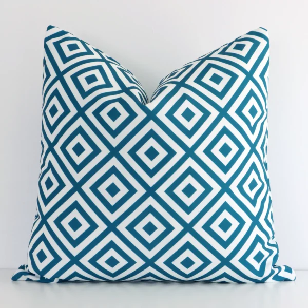 Teal outdoor cushion cover features prominently against a white wall. It is a square design and has a geometric decorative finish.