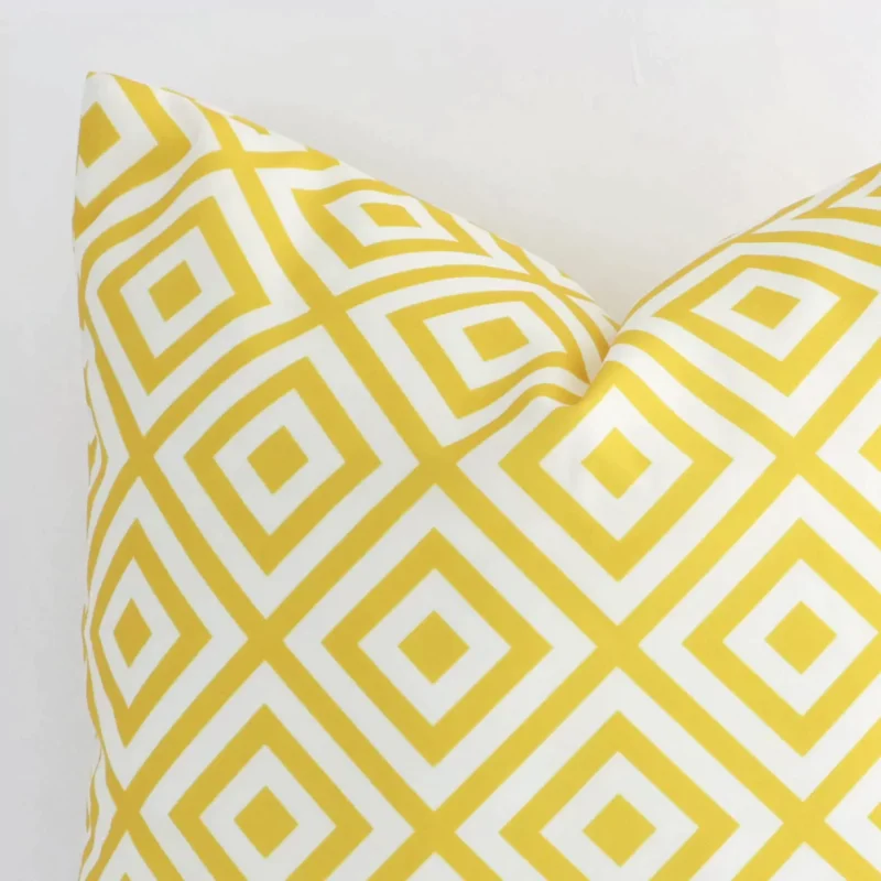 A yellow outdoor cushion cover’s corner is shown in more detail. It is possible to see the square design and geometric decorative finish in much more detail.