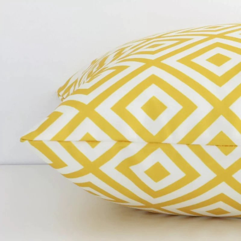 A yellow geometric cushion positioned on its back panel. The shot shows a lateral view of the outdoor fabric and its square shape.
