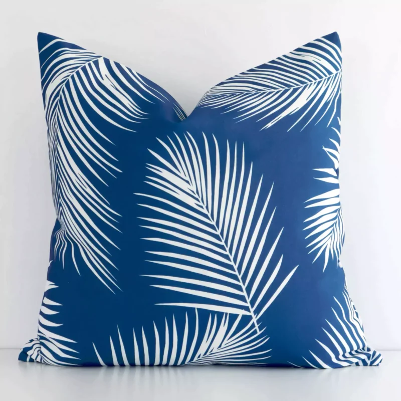 otama-palm-waterproof-blue-outdoor-cushion-cover-sc952-45 A white wall that has a palm designed blue cushion cover positioned in front of it. It has an exquisite outdoor material and a lovely square shape.