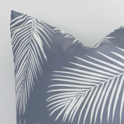 Enlarged shot of the corner of this square palm printed cushion cover in grey colour is shown against a white wall. The image shows the quality and craftsmanship of the outdoor material.