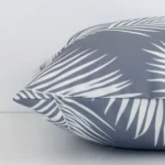 A grey palm printed cushion arranged sideways in front of a wall. The square size and outdoor fabric are shown and the seams are clearly visible.
