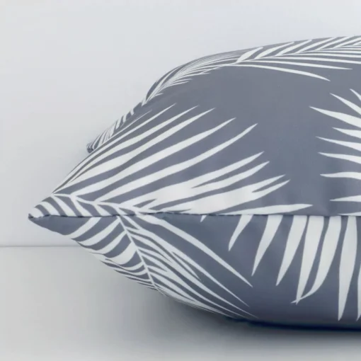 A grey palm printed cushion arranged sideways in front of a wall. The square size and outdoor fabric are shown and the seams are clearly visible.
