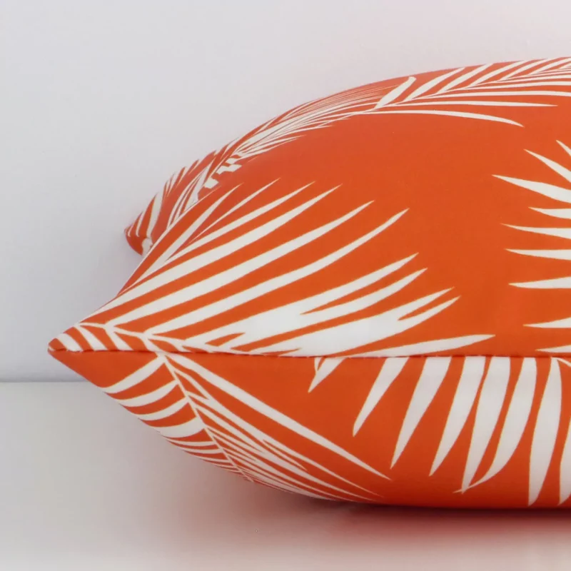 Horizontal edge of palm printed square cushion cover is shown. The outdoor fabric and orange tone can be seen from this side view.