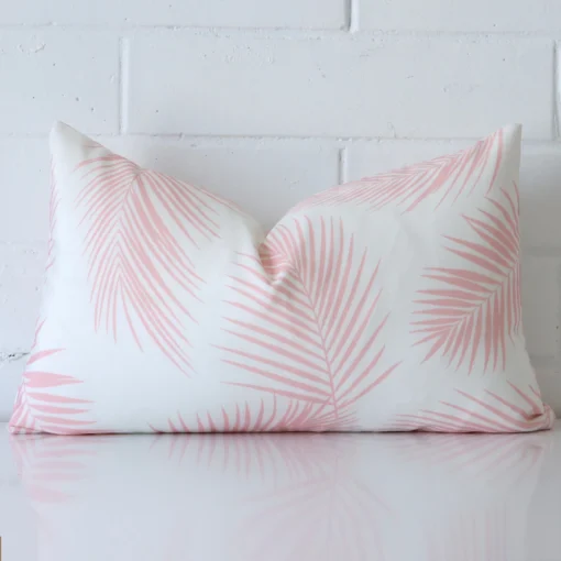 A rectangle cushion in a delightful pink tone rests against a white wall. The outdoor material appears to be of exceptional quality.