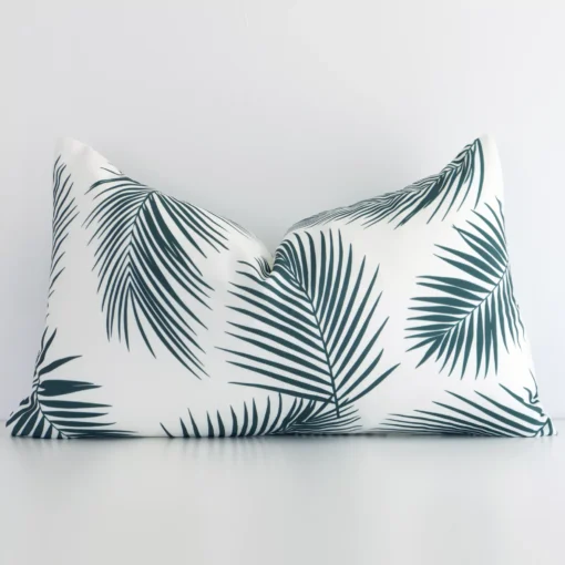 Here a green outdoor cushion is shown styled against a white wall. It has a rectangular design and features a palm style.