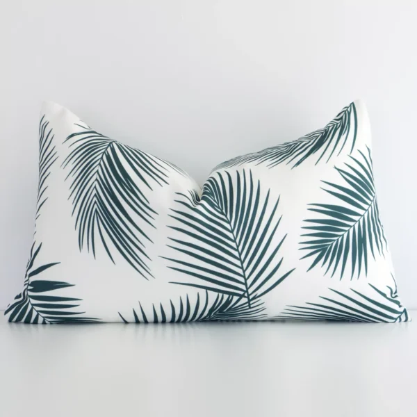 Here a green outdoor cushion is shown styled against a white wall. It has a rectangular design and features a palm style.