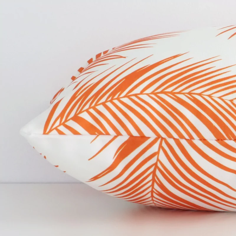 Lateral angle image of an outdoor rectangle cushion. The orange colour and palm design are highlighted along its seams.