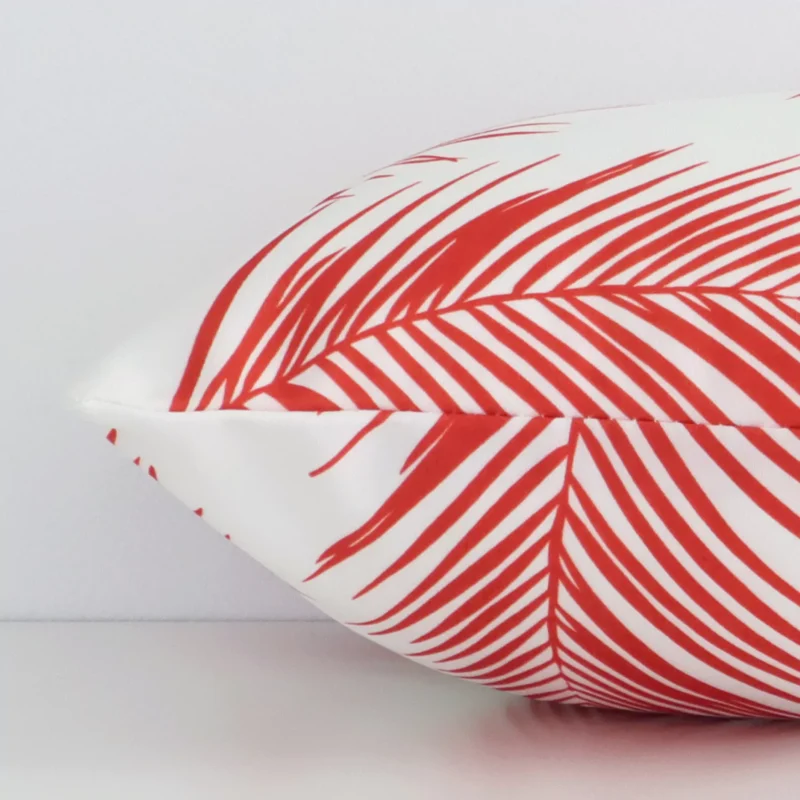 Horizontal edge view of front and back panels of a red palm printed outdoor cushion in a rectangle size.