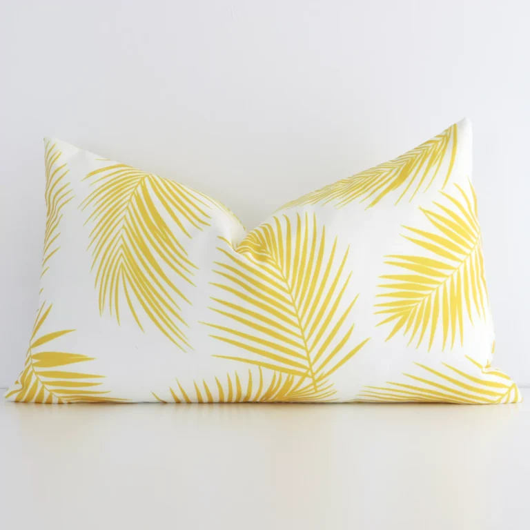 Yellow palm printed cushion leans elegantly against a white wall. It has been crafted from a high quality outdoor material and has a rectangle shape.