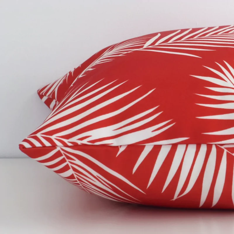 A square outdoor cushion positioned flat to show its seams. The red colour and palm design are visible as is the seam between the panels.