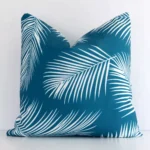 A white wall that has a teal cushion cover positioned in front of it. It has an exquisite outdoor material and a lovely square shape.