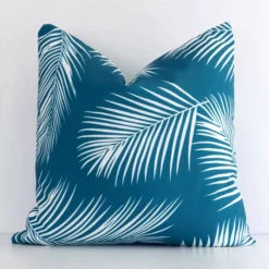 A white wall that has a teal cushion cover positioned in front of it. It has an exquisite outdoor material and a lovely square shape.