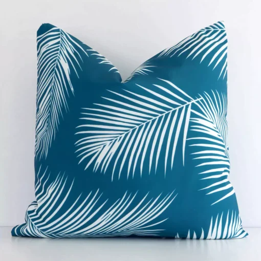 A white wall that has a teal cushion cover positioned in front of it. It has an exquisite outdoor material and a lovely square shape.